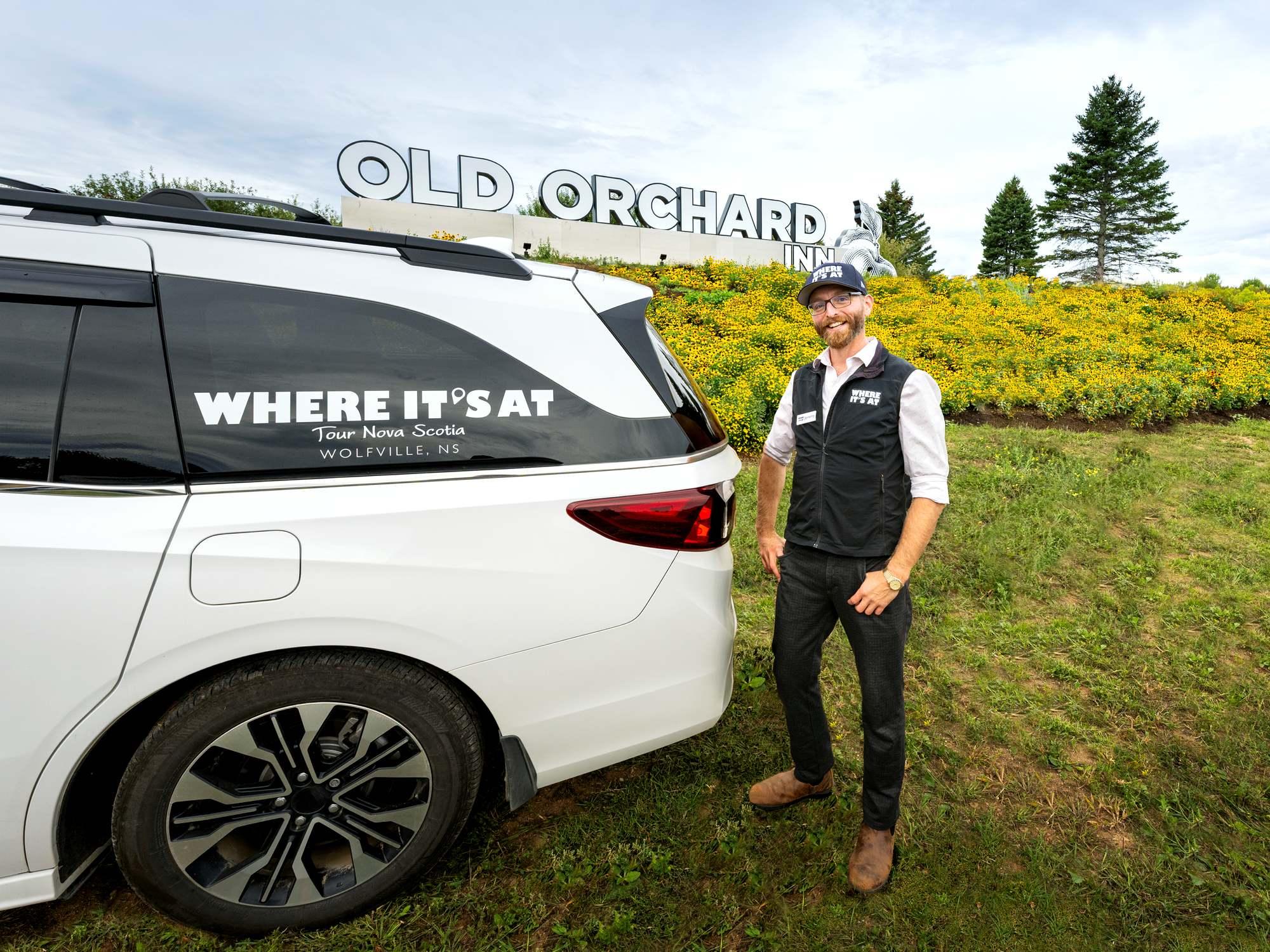 Tour operator guide stands beside a white van in front of the Old Orchard Inn sign