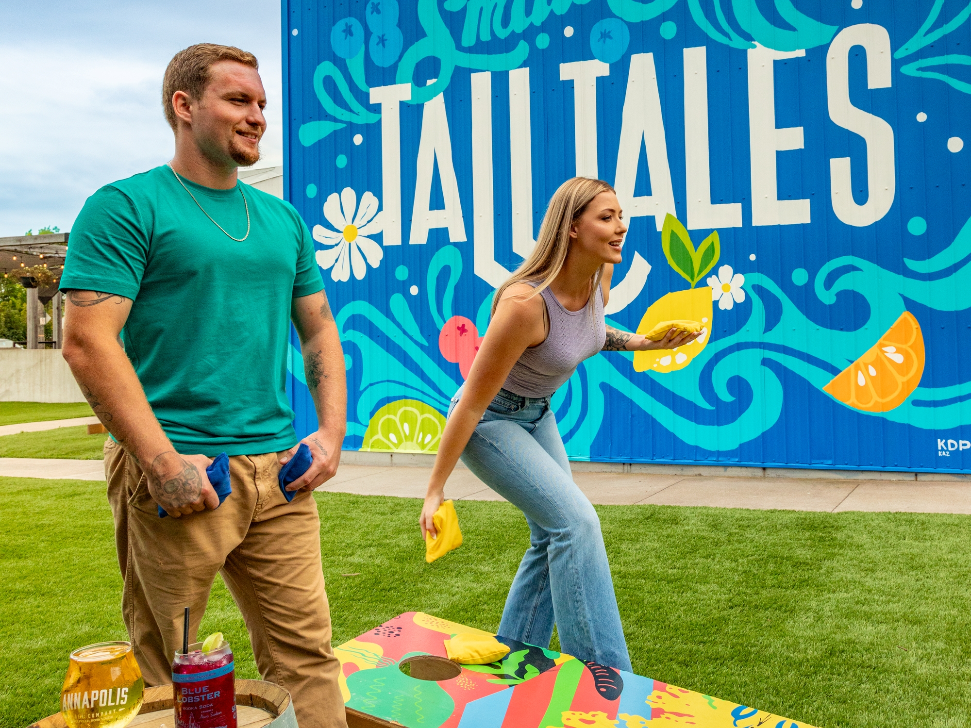 People engaged in a game of cornhole in front of a bright mural