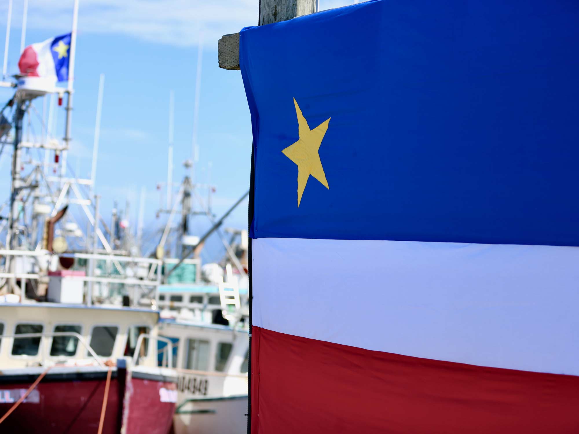 Acadian flag next to fishing boats that also have Acadian flags on them in Nova Scotia.