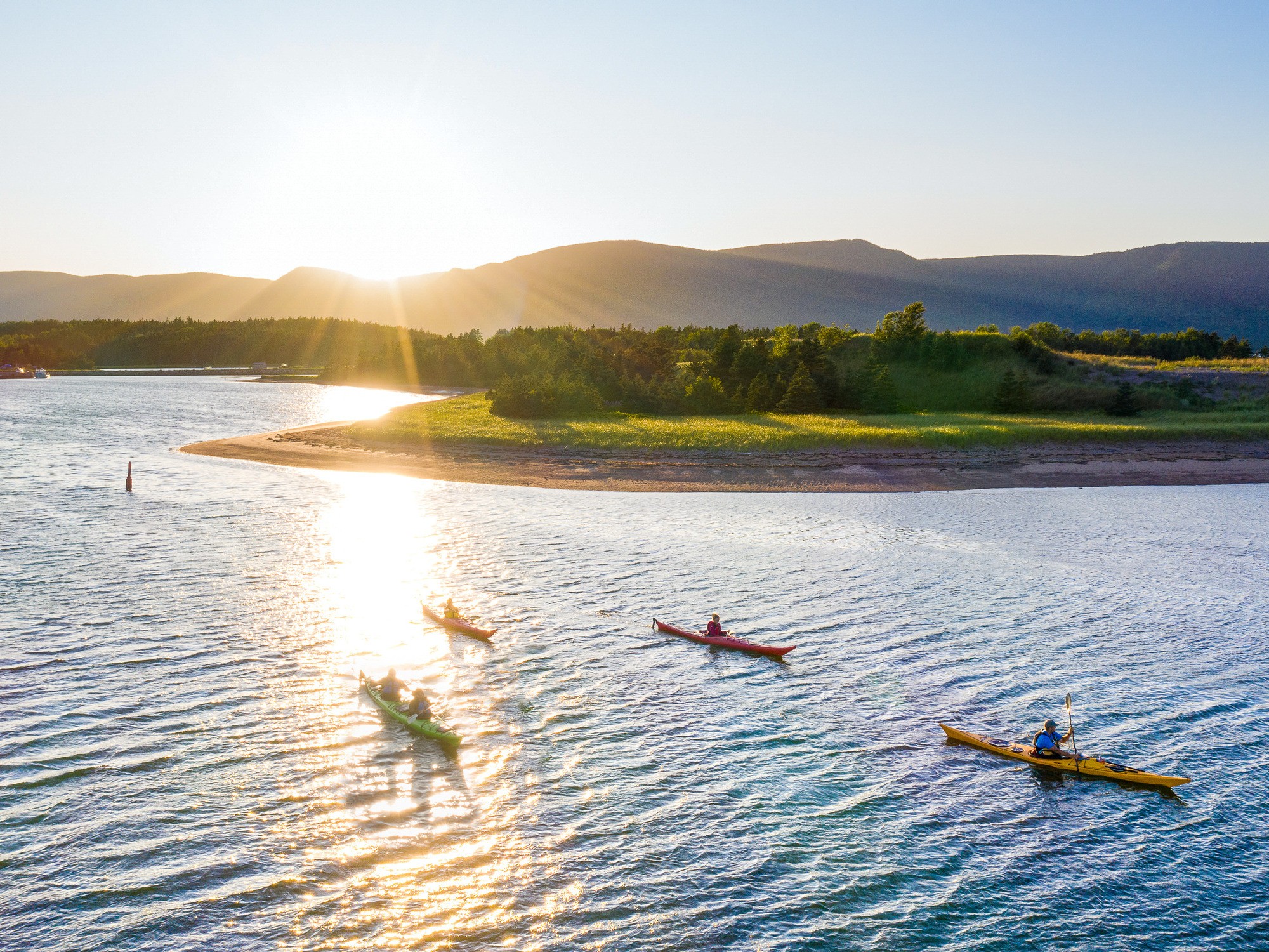 Kayakers in Dingwall harbour with highlands rising behind them on Cape Breton Island in Nova Scotia