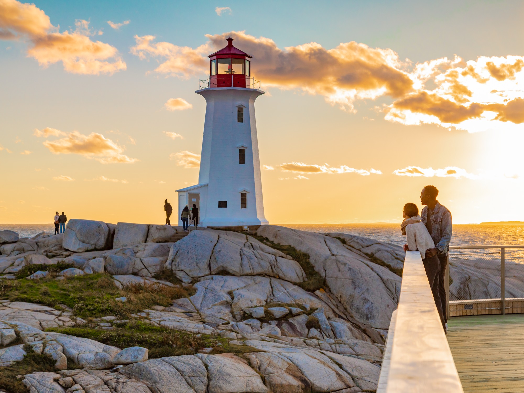 Two people stand on the viewing deck at Peggy's Cove at sunset