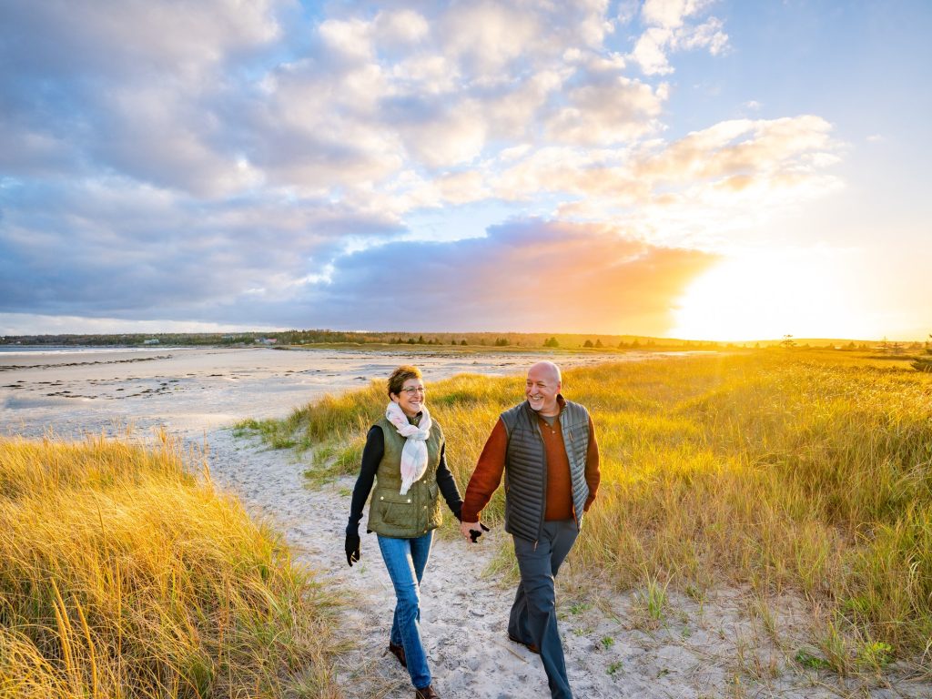 Two people walk along a path at Roseway Beach in Shelburne, Nova Scotia during fall.
