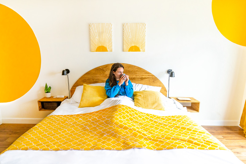 A woman relaxing with a cup of coffee in a brightly coloured guestroom at The Marmalade Motel in Port Dufferin, Nova Scotia.