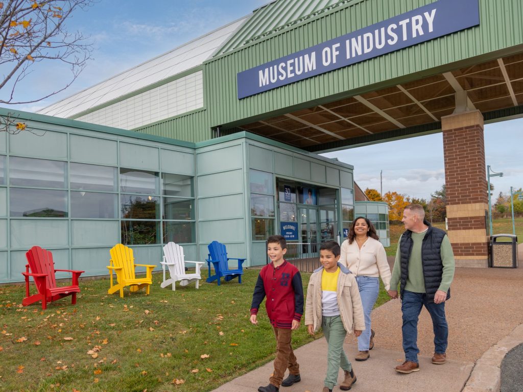A family of four walking past colourful chairs in front of the Museum of Industry