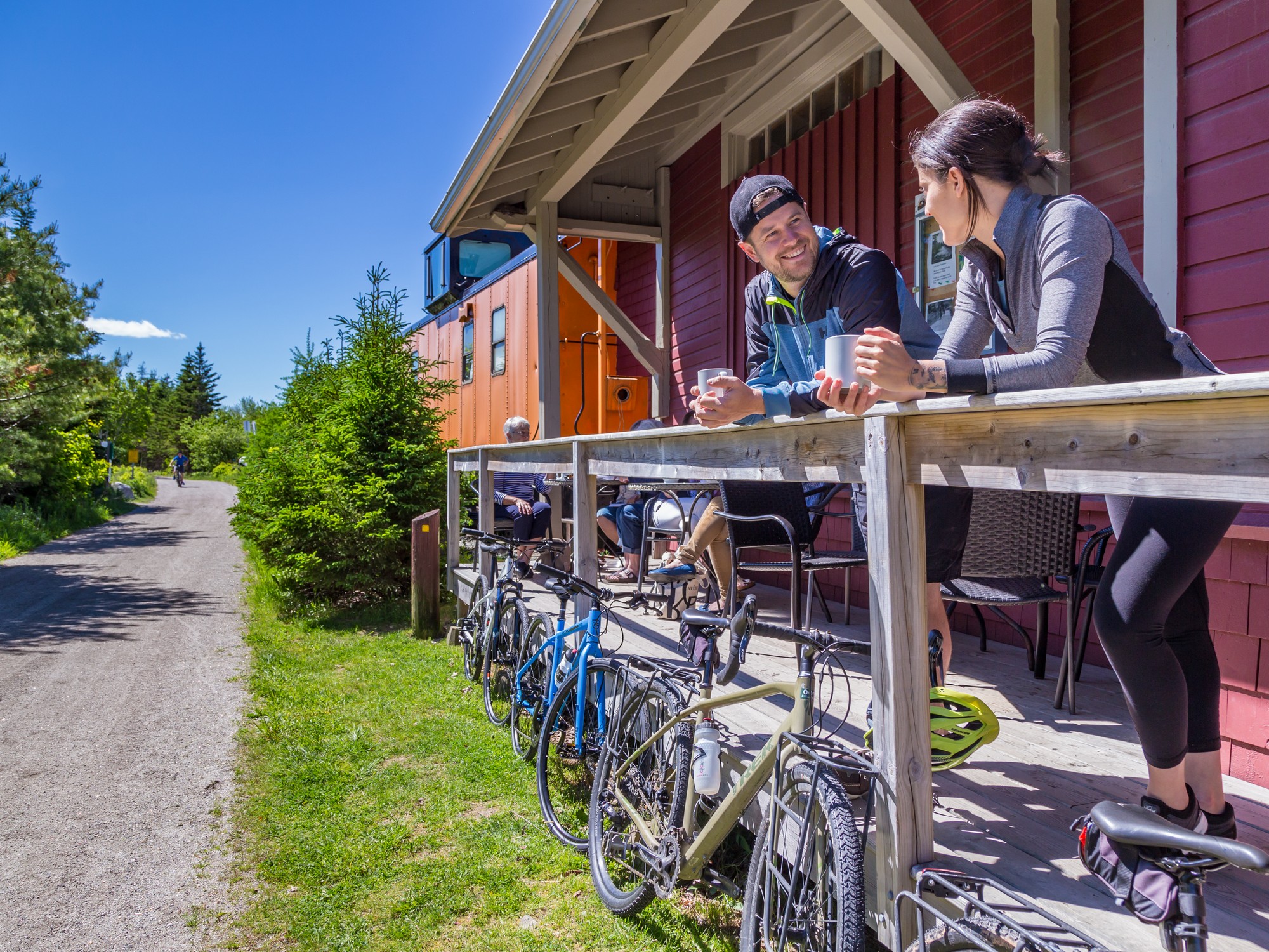 Two people enjoy coffee on a patio overlooking a trail at the Train Station Bike & Bean in Nova Scotia